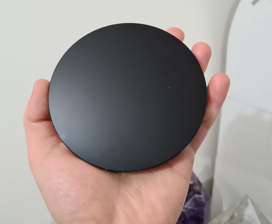 A hand holding a Black Obsidian crystal scrying mirror that is 10 centimetres in size