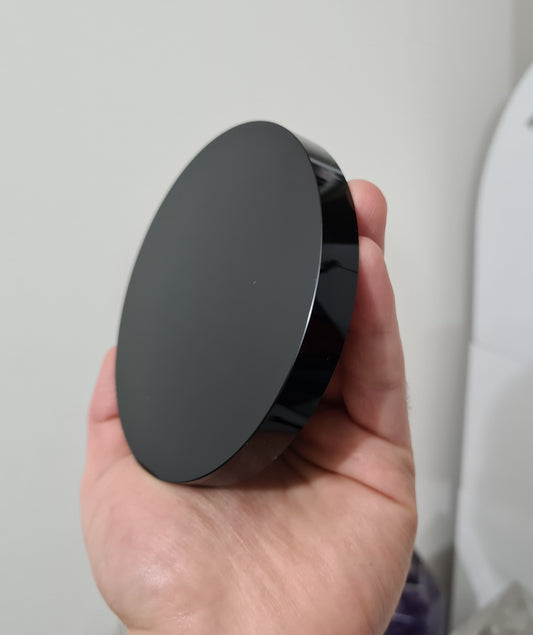 A hand holding a Black Obsidian crystal scrying mirror that is 10 centimetres in size