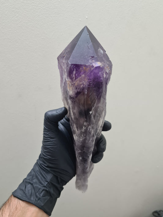 A gloved hand holding a large purple Amethyst crystal sceptre that is approximately 25 centimetres by 7.5 centimetres in size