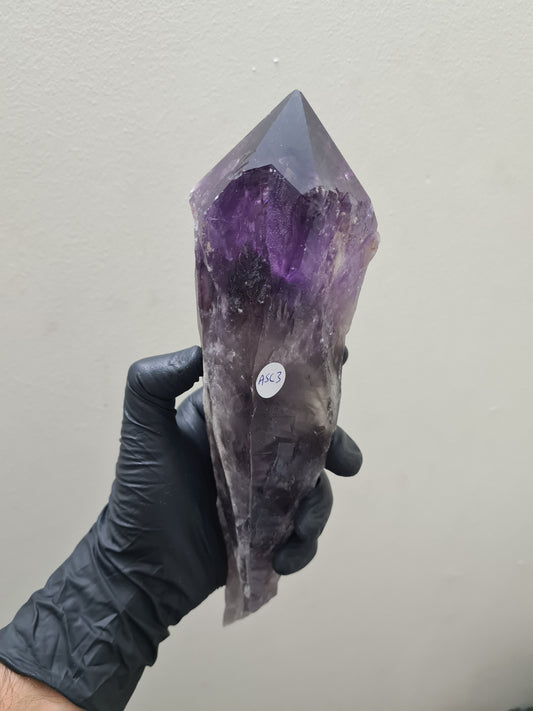 A gloved hand holding a large purple Amethyst crystal sceptre that is approximately 25 centimetres by 7.5 centimetres in size