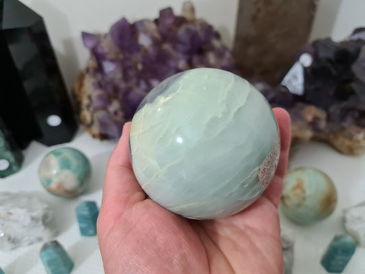 A hand holding a polished Caribbean Calcite with Pyrite crystal sphere that is approximately 7.5 centimetres in size