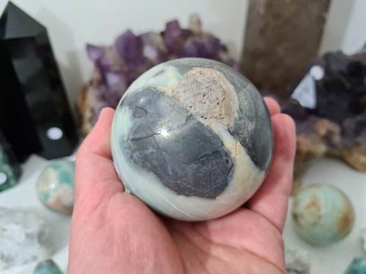 A hand holding a polished Caribbean Calcite with Pyrite crystal sphere that is approximately 7.5 centimetres in size