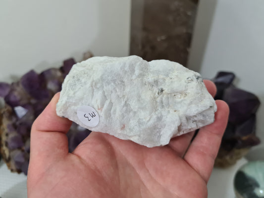 A hand holding a natural Rainbow Moonstone crystal piece that is approximately 10 centimetres by 6 centimetres in size