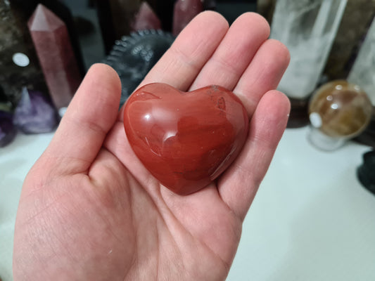 A hand holding a Mookaite crystal heart that is approximately 5 centimetres by 5 centimetres in size