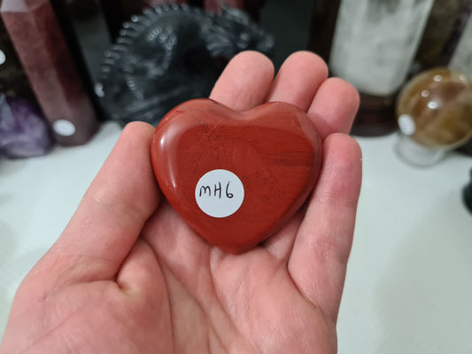 A hand holding a Mookaite crystal heart that is approximately 5 centimetres by 5 centimetres in size