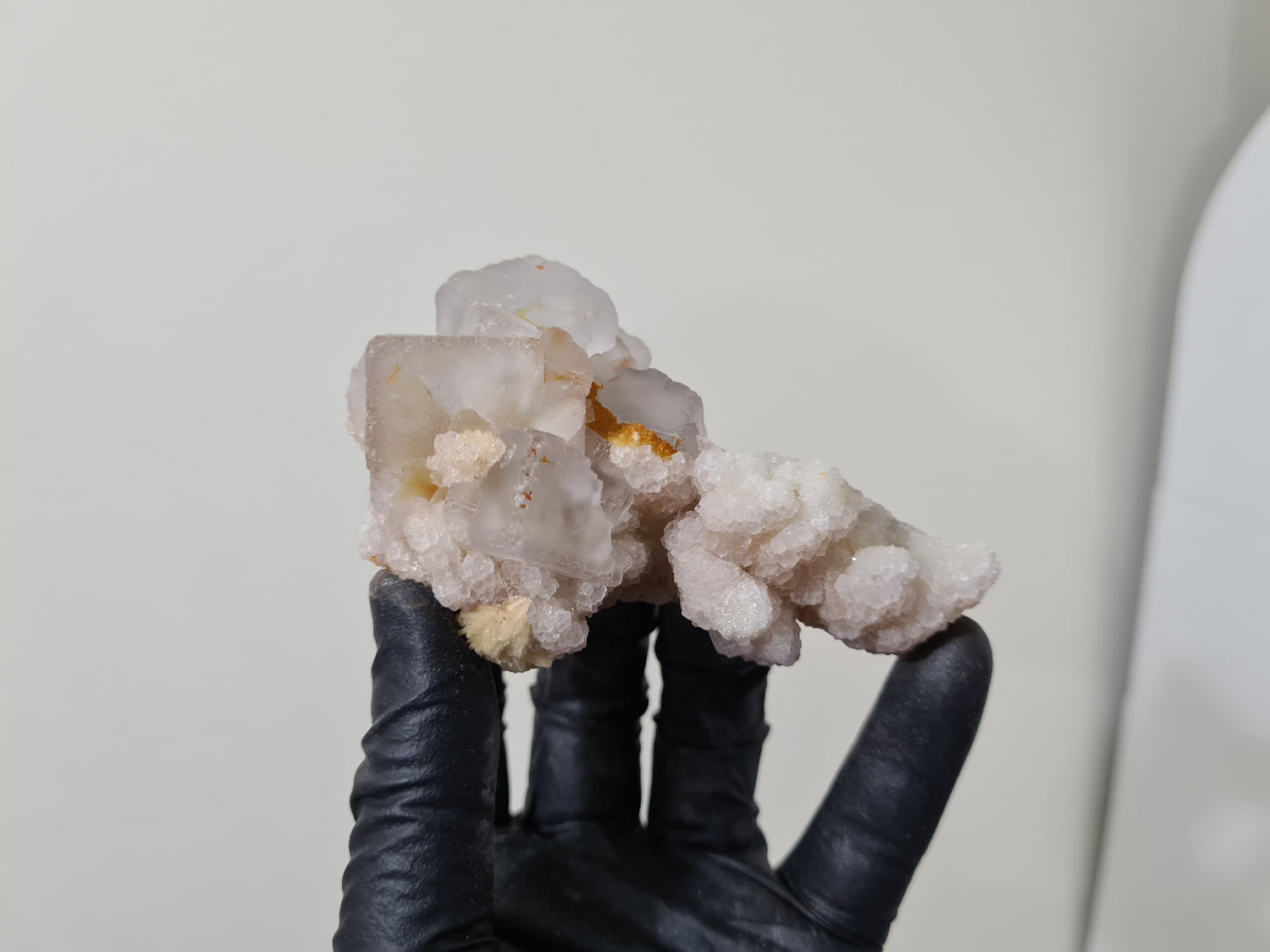 A gloved hand holding a natural Fluorite crystal that is approximately 9.5 centimetres by 6 centimetres in size