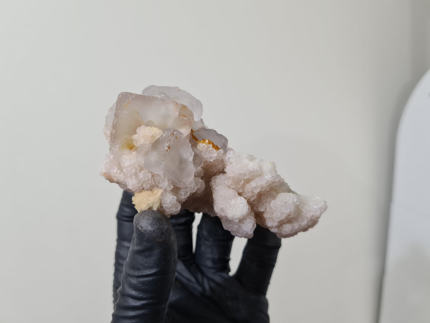 A gloved hand holding a natural Fluorite crystal that is approximately 9.5 centimetres by 6 centimetres in size