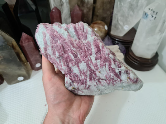 A hand holding a large natural Pink Tourmaline crystal that is approximately 20cm by 10cm in size