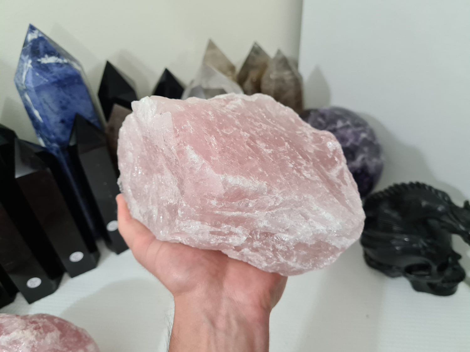 A hand holding a large natural Rose Quartz crystal that is approximately 18 centimetres by 14 centimetres in size