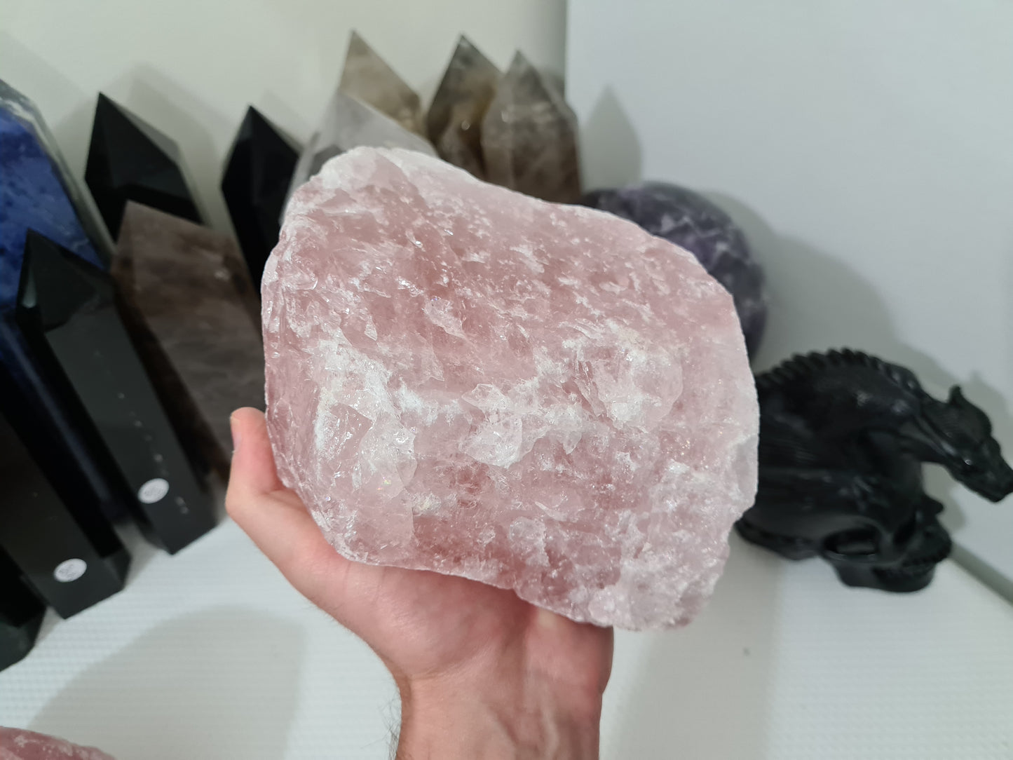 A hand holding a large natural Rose Quartz crystal that is approximately 18 centimetres by 14 centimetres in size