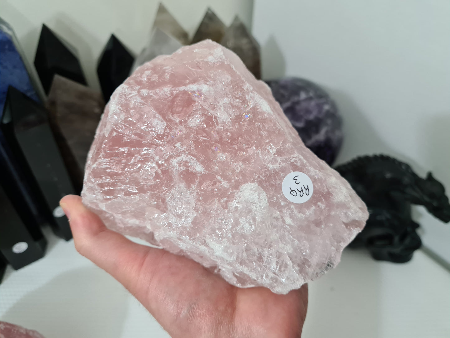 A hand holding a large natural Rose Quartz crystal that is approximately 18 centimetres by 14 centimetres in size