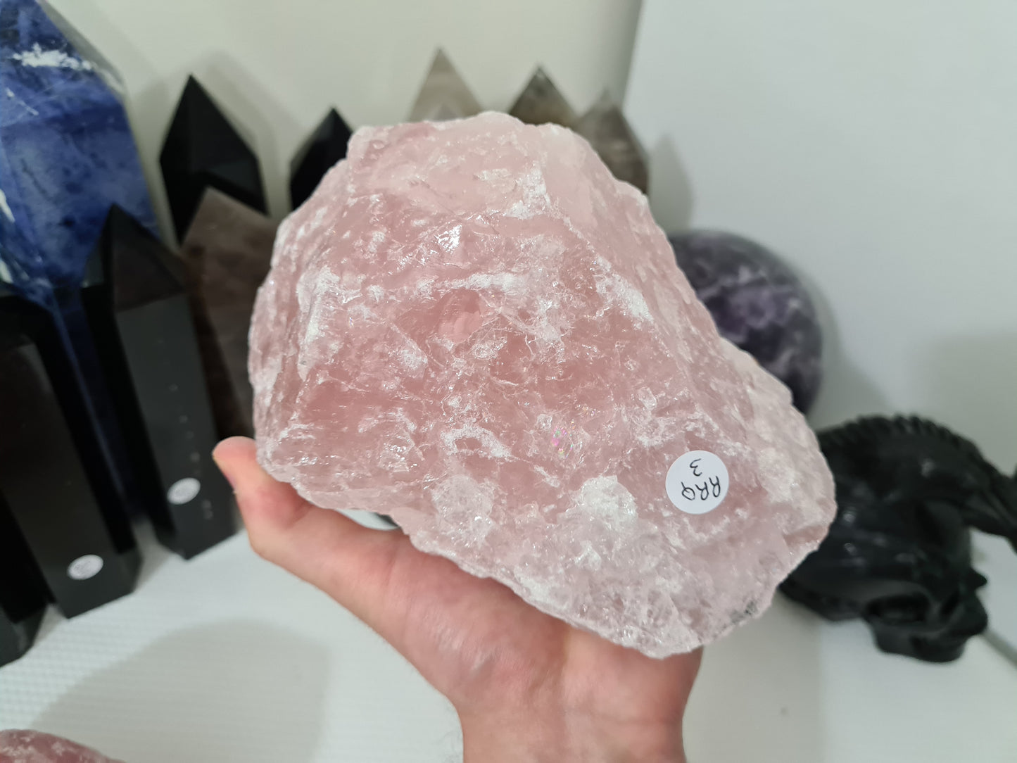 A hand holding a large natural Rose Quartz crystal that is approximately 18 centimetres by 14 centimetres in size