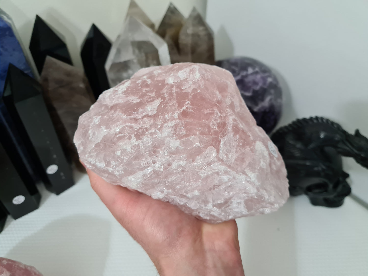 A hand holding a large natural Rose Quartz crystal that is approximately 18 centimetres by 14 centimetres in size