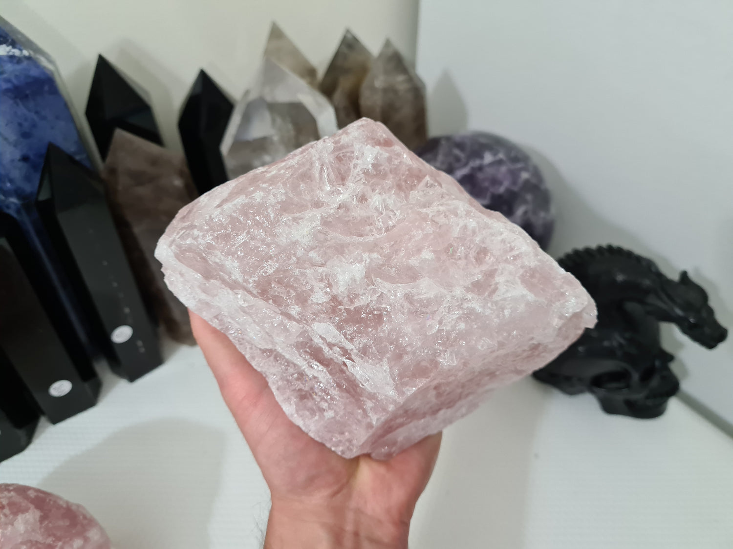 A hand holding a large natural Rose Quartz crystal that is approximately 18 centimetres by 14 centimetres in size