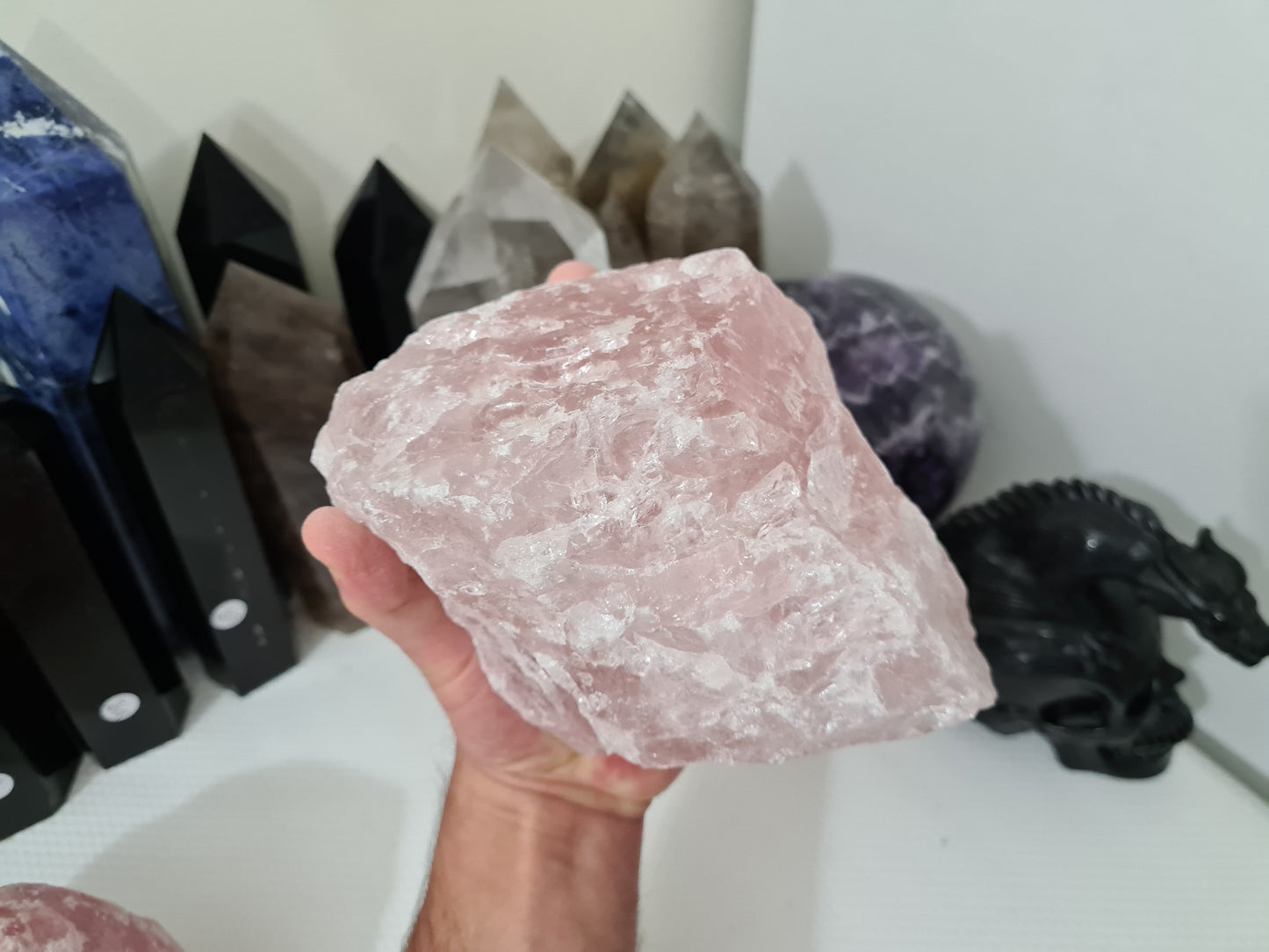 A hand holding a large natural Rose Quartz crystal that is approximately 18 centimetres by 14 centimetres in size