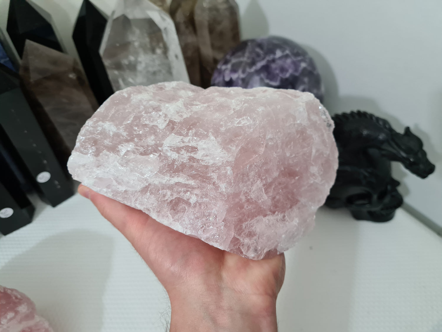 A hand holding a large natural Rose Quartz crystal that is approximately 18 centimetres by 14 centimetres in size