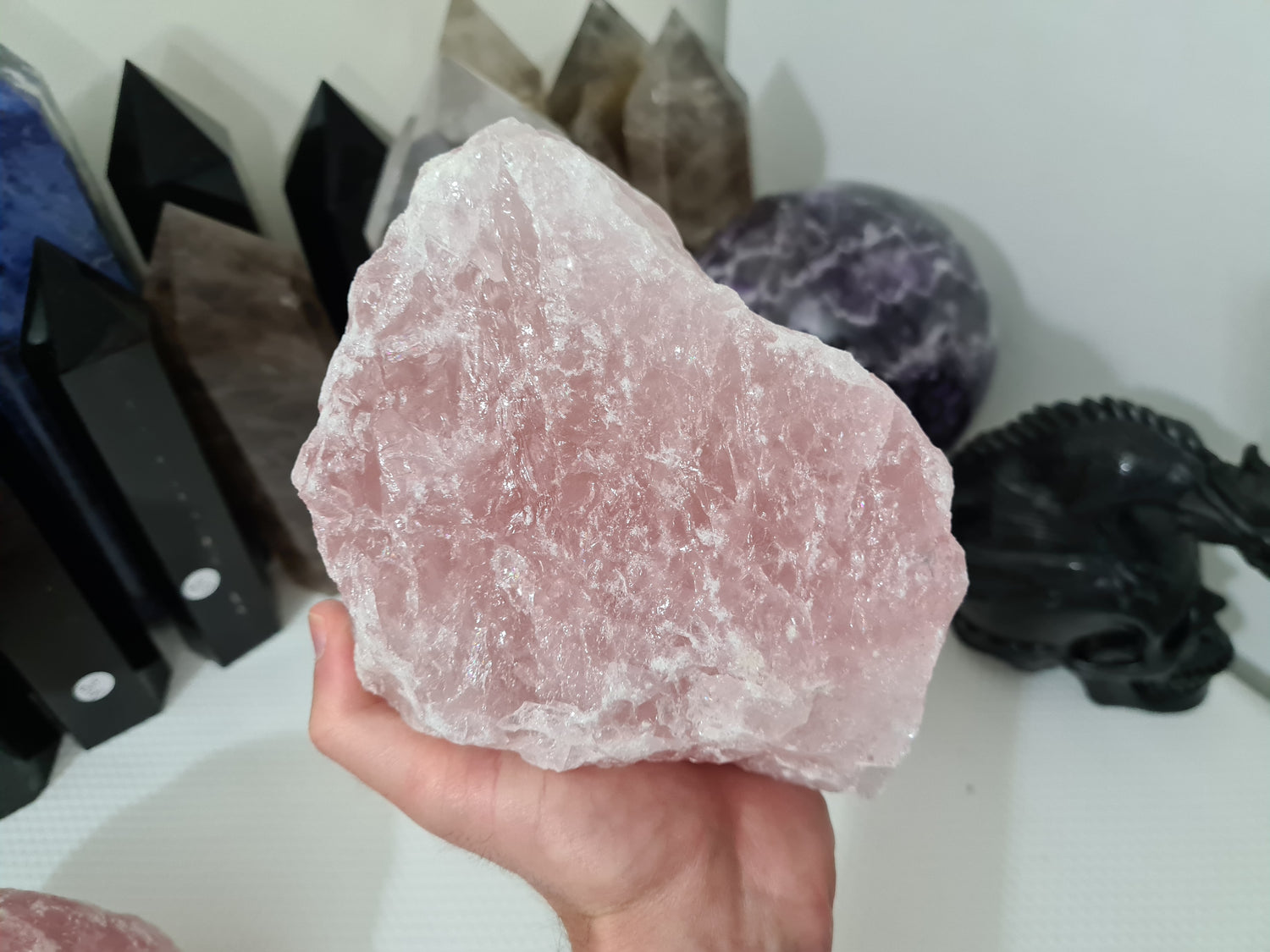 A hand holding a large natural Rose Quartz crystal that is approximately 18 centimetres by 14 centimetres in size