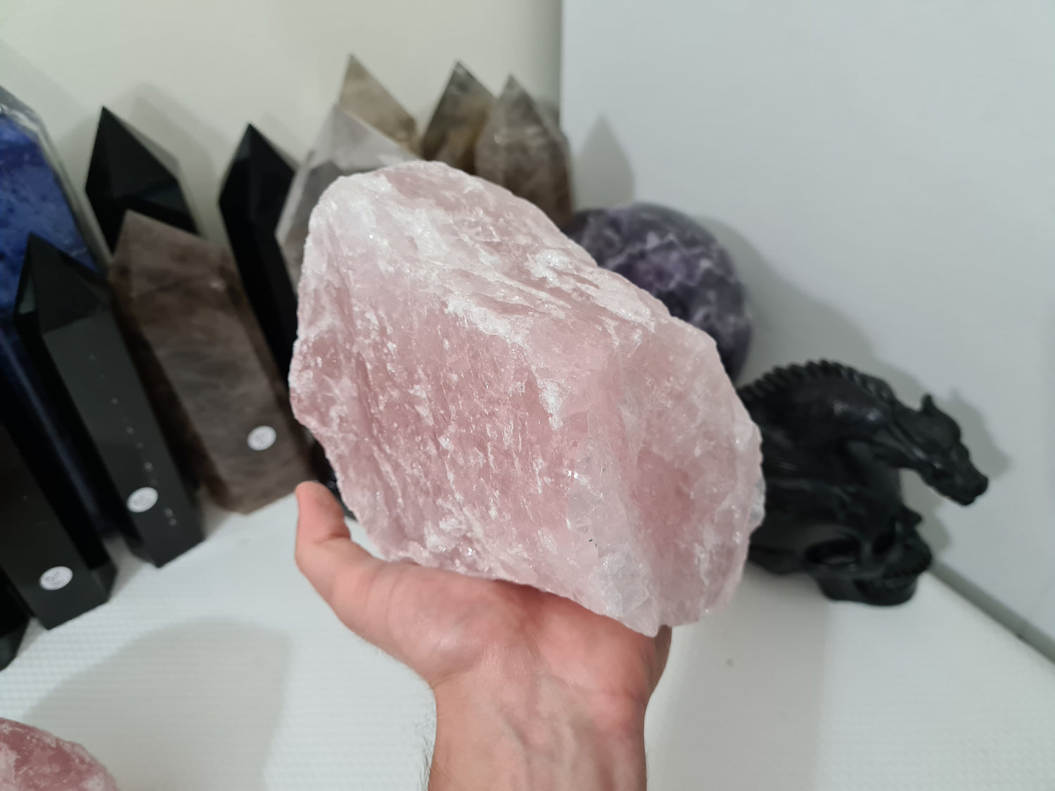 A hand holding a large natural Rose Quartz crystal that is approximately 18 centimetres by 14 centimetres in size