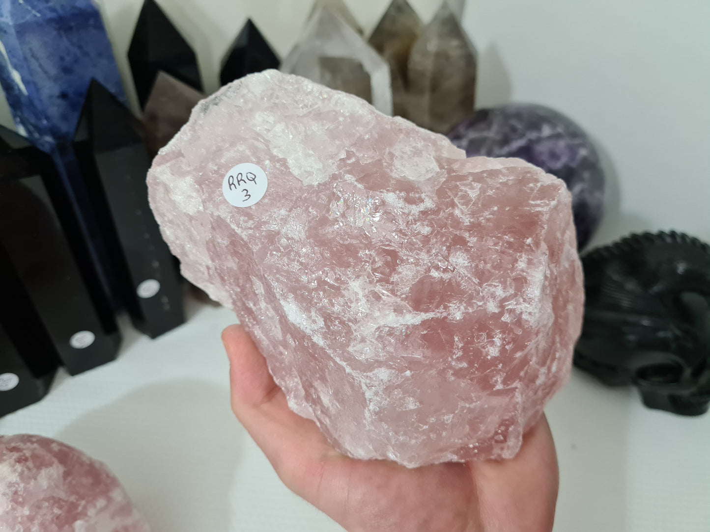 A hand holding a large natural Rose Quartz crystal that is approximately 18 centimetres by 14 centimetres in size