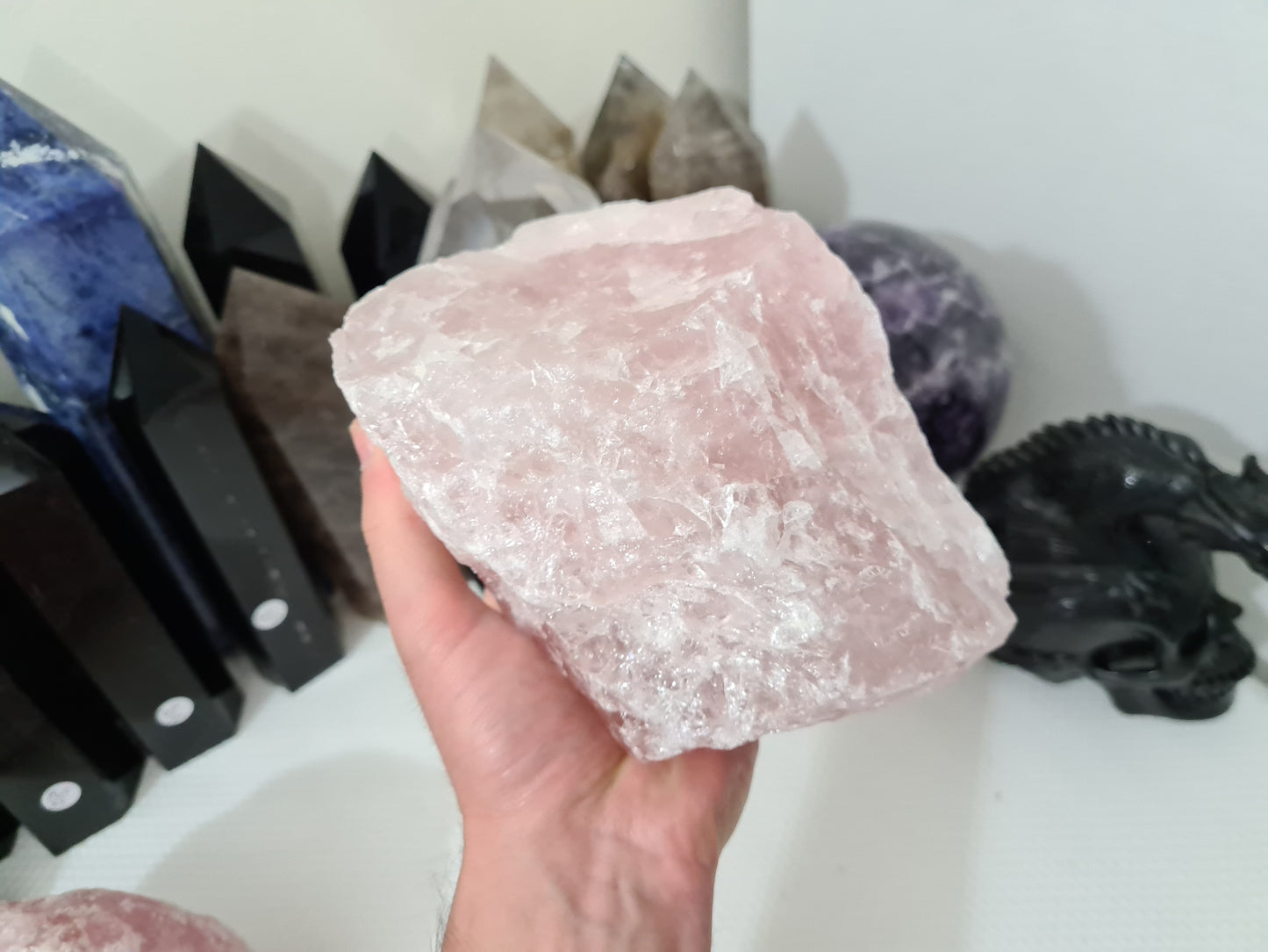 A hand holding a large natural Rose Quartz crystal that is approximately 18 centimetres by 14 centimetres in size