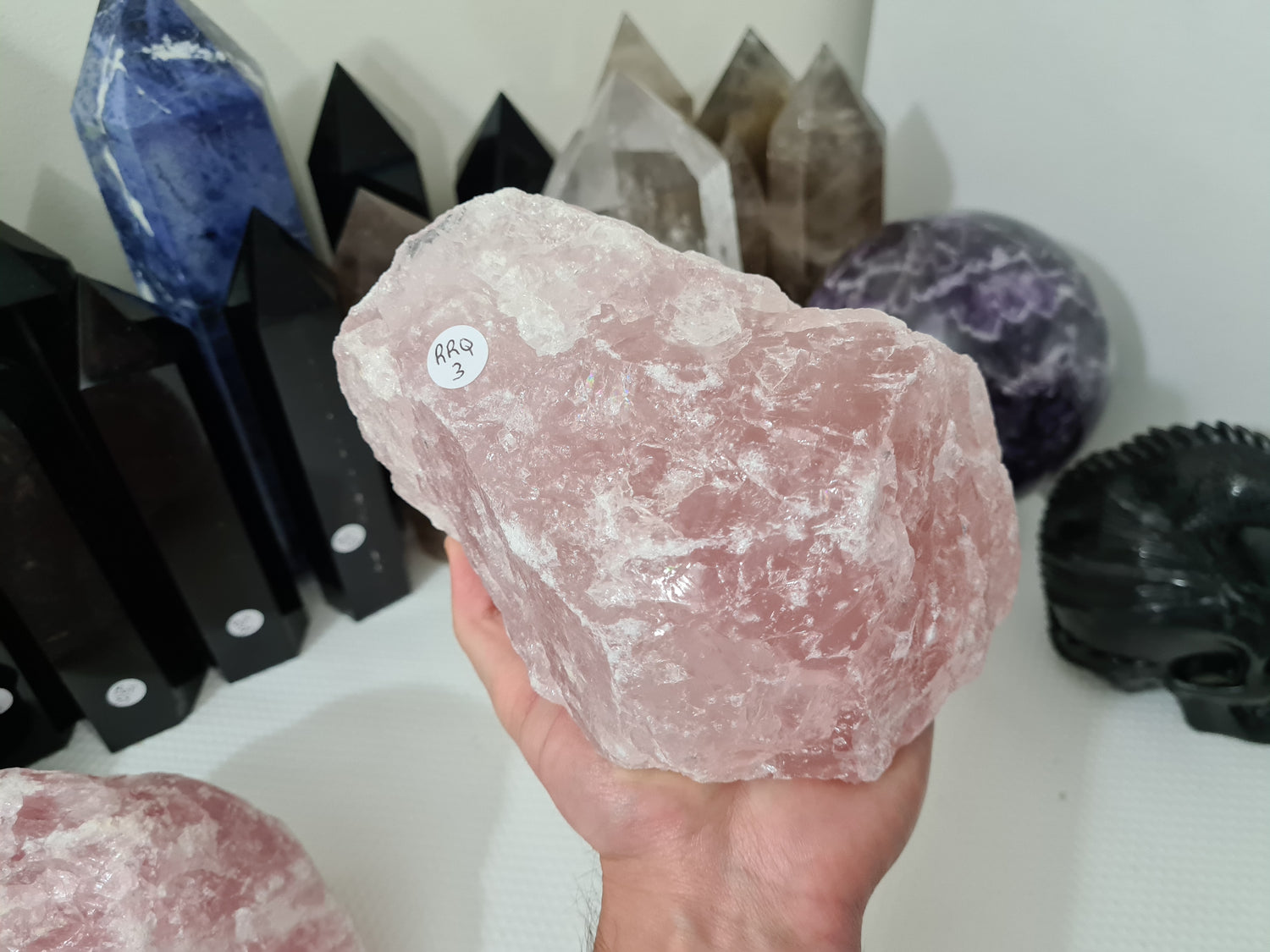 A hand holding a large natural Rose Quartz crystal that is approximately 18 centimetres by 14 centimetres in size