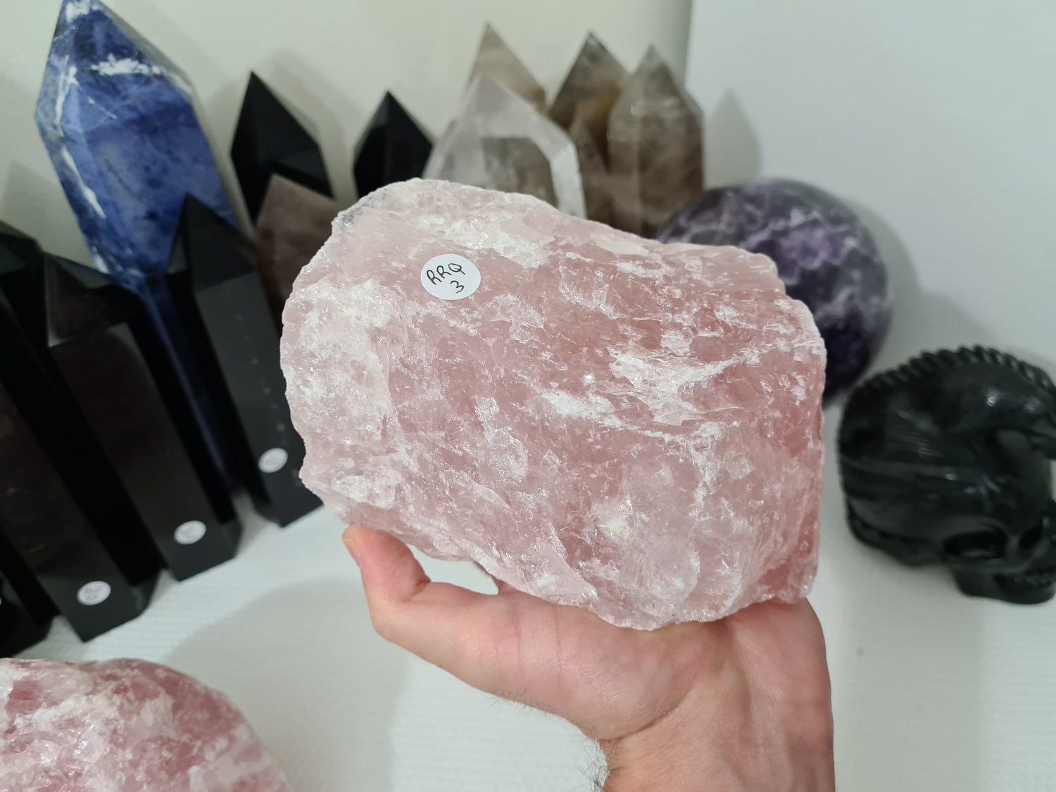 A hand holding a large natural Rose Quartz crystal that is approximately 18 centimetres by 14 centimetres in size