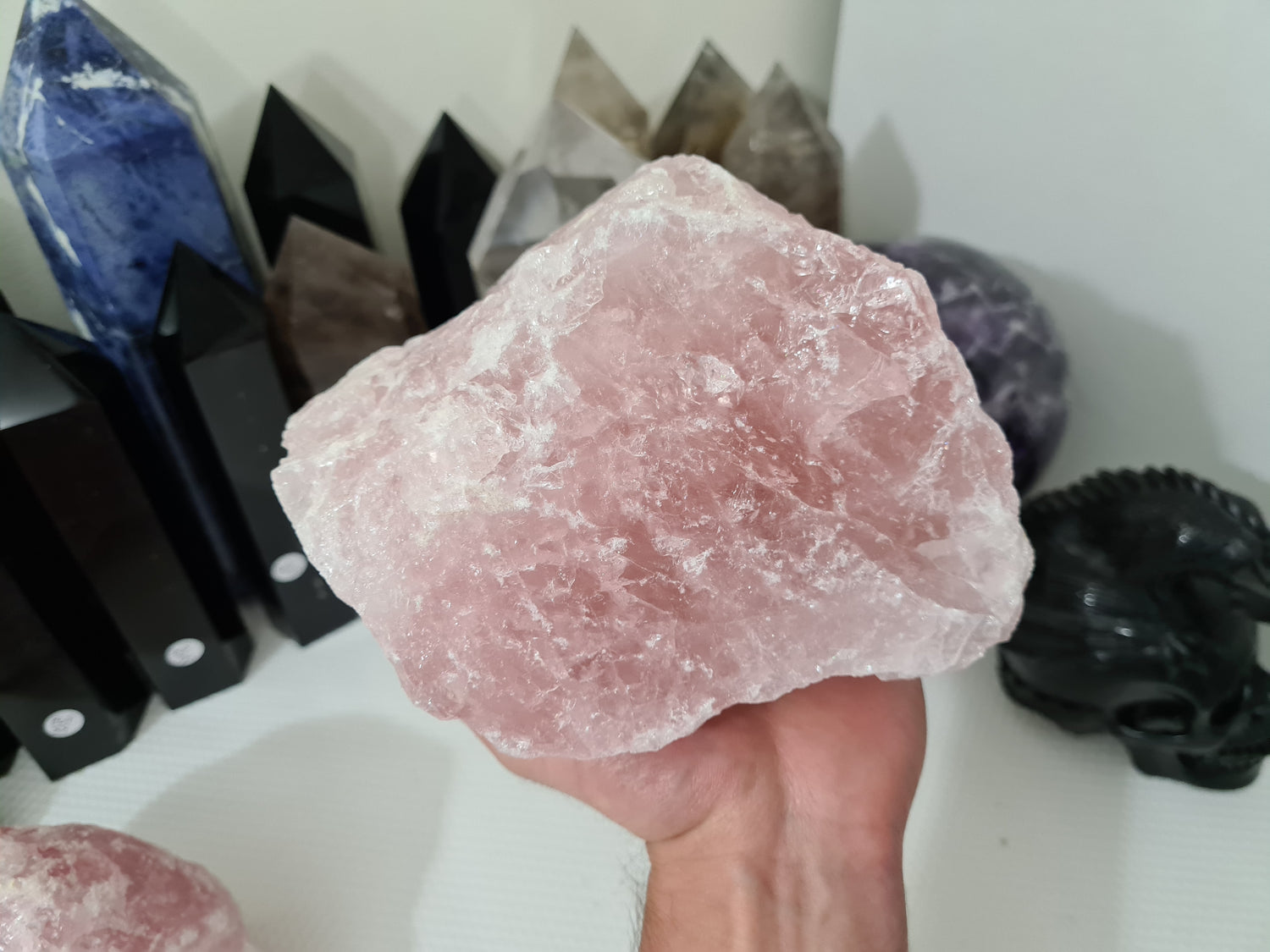 A hand holding a large natural Rose Quartz crystal that is approximately 18 centimetres by 14 centimetres in size