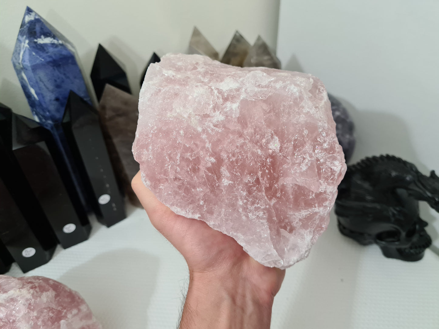 A hand holding a large natural Rose Quartz crystal that is approximately 18 centimetres by 14 centimetres in size