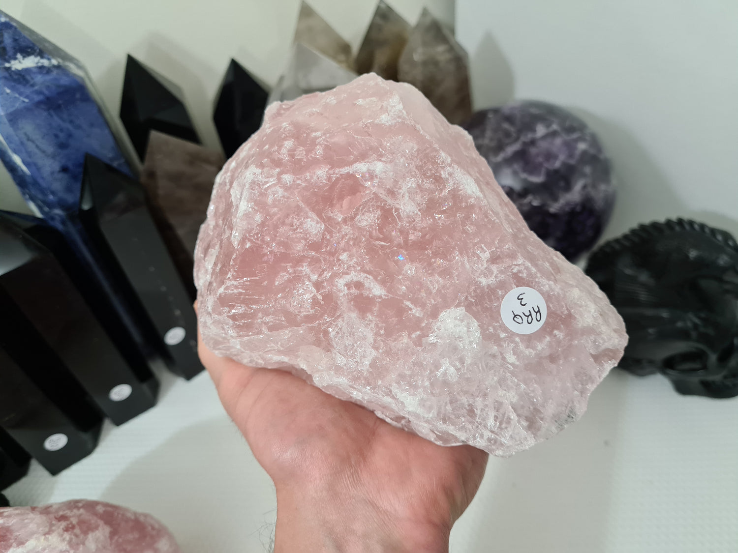 A hand holding a large natural Rose Quartz crystal that is approximately 18 centimetres by 14 centimetres in size