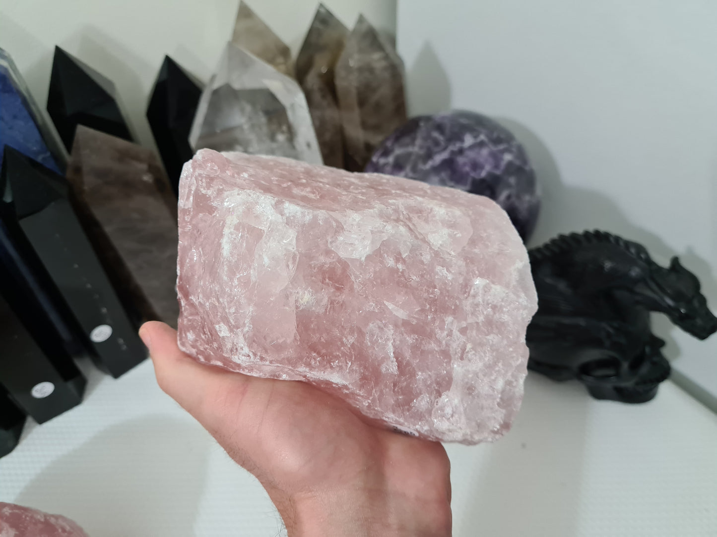 A hand holding a large natural Rose Quartz crystal that is approximately 18 centimetres by 14 centimetres in size