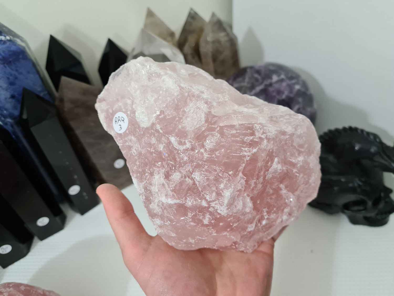 A hand holding a large natural Rose Quartz crystal that is approximately 18 centimetres by 14 centimetres in size