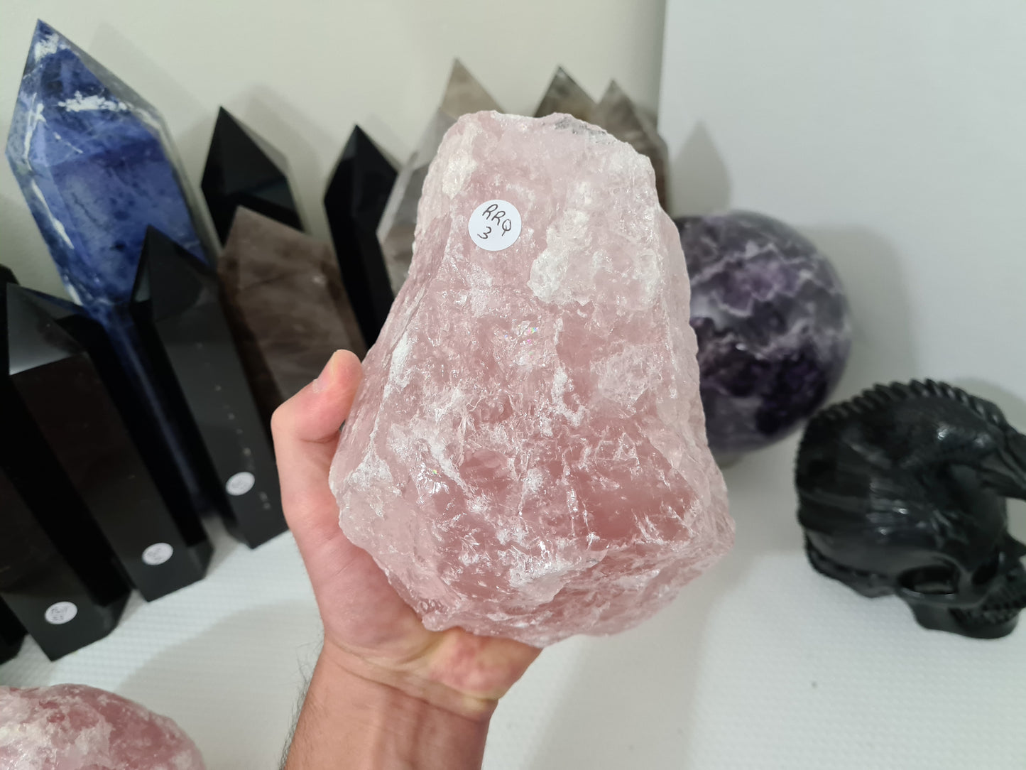 A hand holding a large natural Rose Quartz crystal that is approximately 18 centimetres by 14 centimetres in size