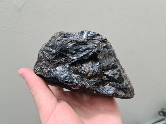 A hand holding a natural Smoky Quartz crystal chunk that is approximately 12.5 centimetres by 8.5 centimetres in size