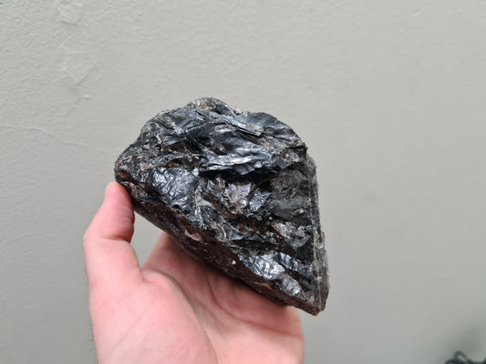 A hand holding a natural Smoky Quartz crystal chunk that is approximately 12.5 centimetres by 8.5 centimetres in size